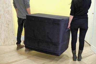 Deux personnes portent le cube avec les poignées de côté.