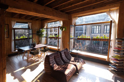 A living room with 3 bigs windows and 2 planters on each one of them.